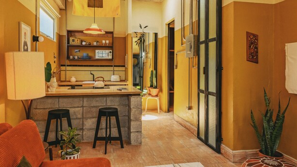 Una cocina compacta con una isla central, taburetes de bar y una lámpara colgante.