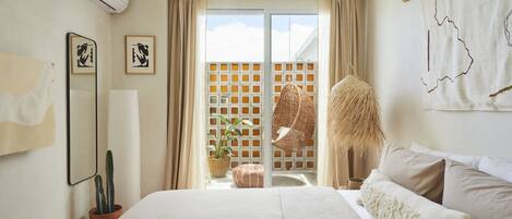 A bedroom with a large bed, a potted plant, a hanging chair, and a view of the outside.