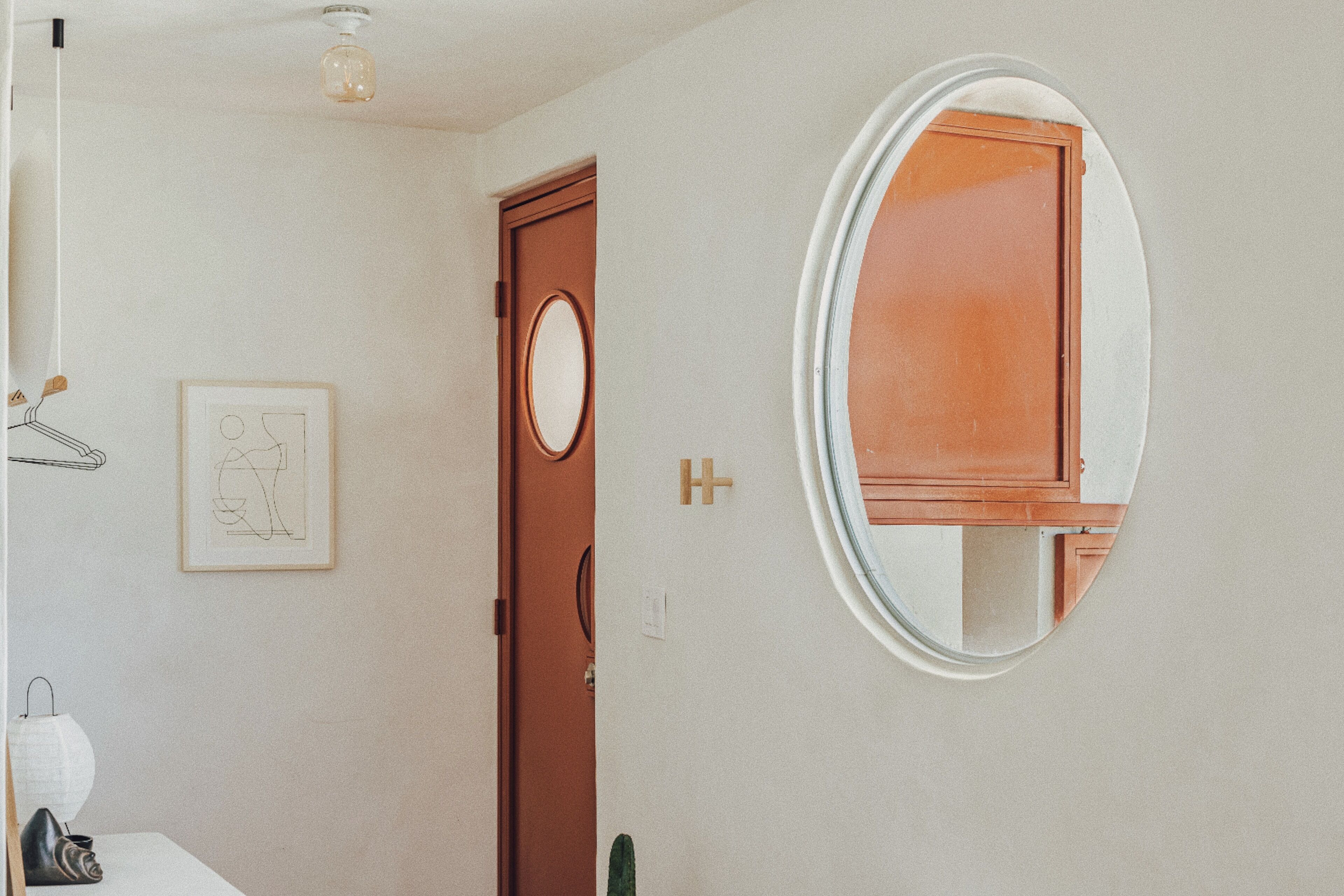 A bathroom with a wooden door, a round mirror, and a framed picture on the wall.