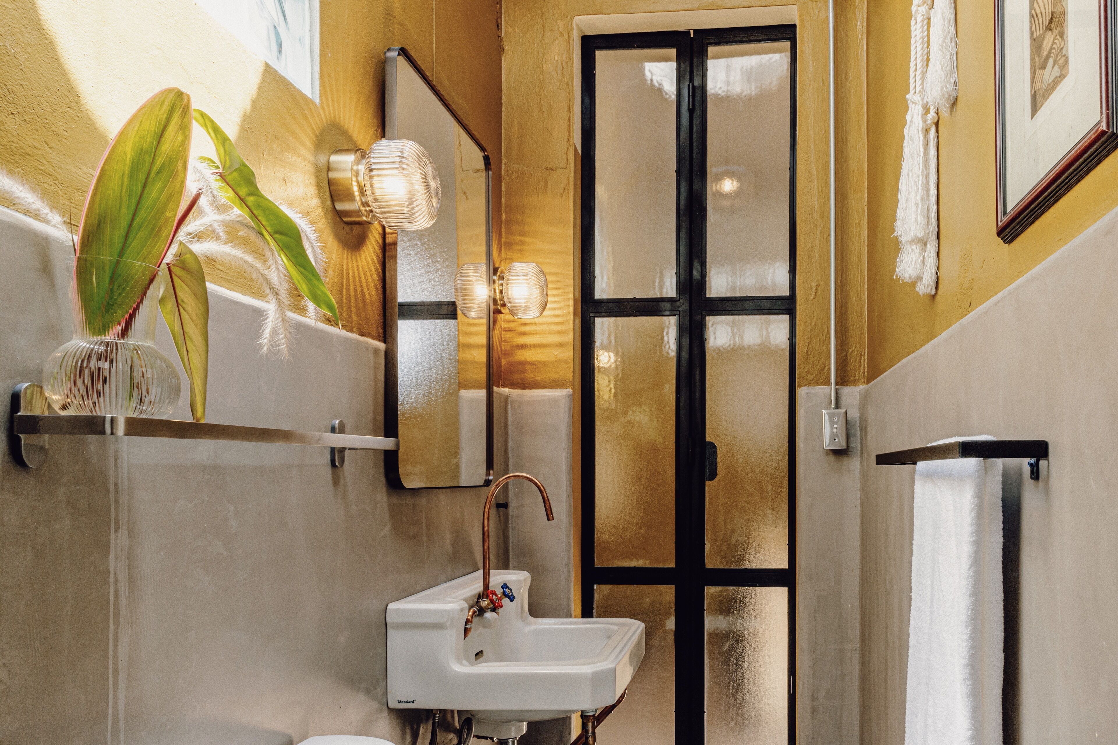 Ein Badezimmer mit einem weißen Waschbecken, einem Spiegel und einer Pflanze.