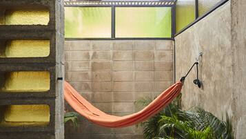 A hammock suspended between a concrete wall and a glass partition, with a view of a tiled floor and green plants.