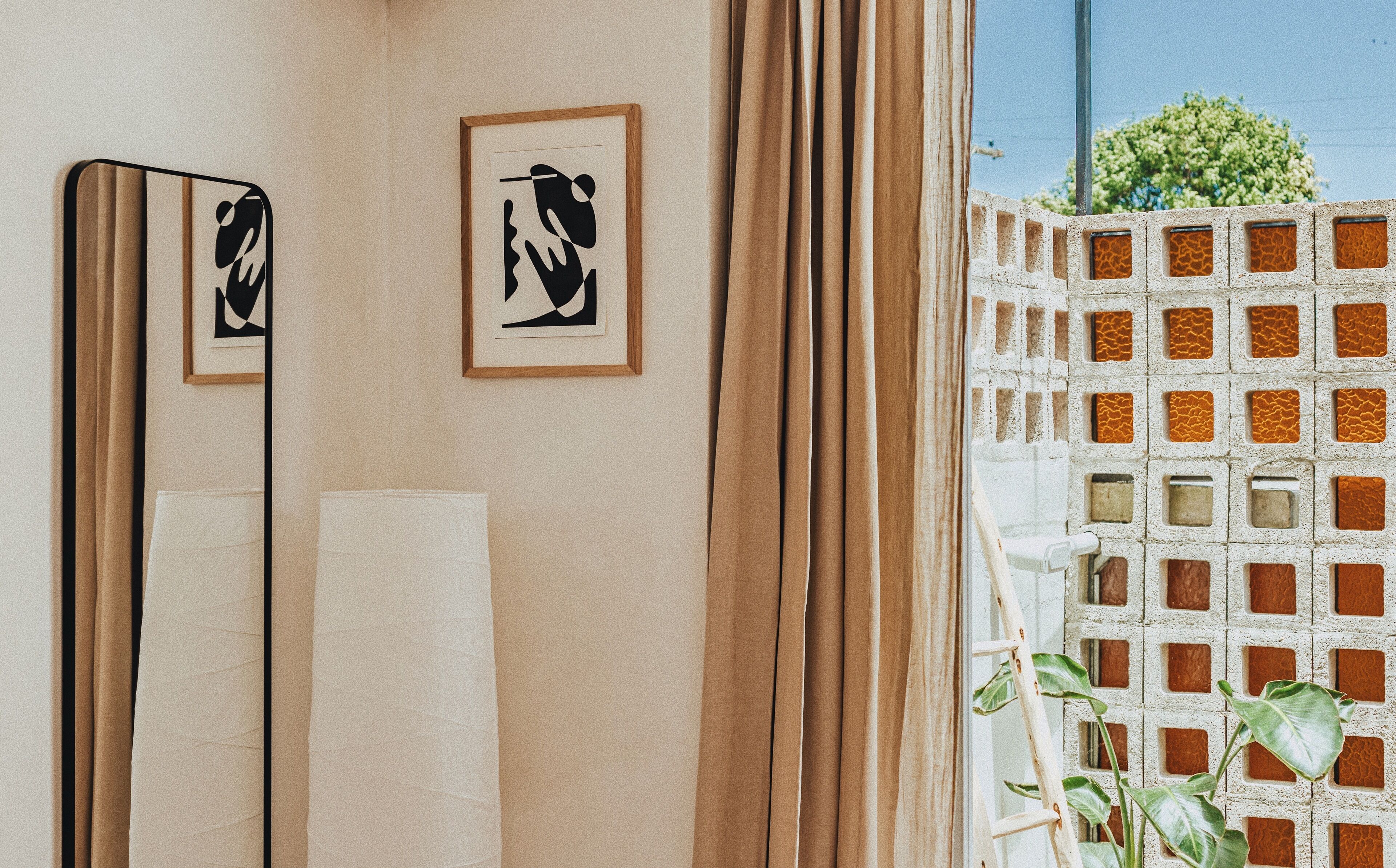 A bathroom with a large mirror, two framed artworks, a towel, and a view of a brick wall with a plant outside.