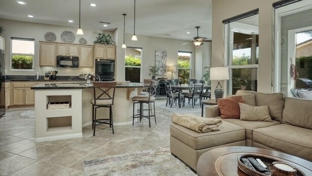 A spacious kitchen with a central island, dining area with chairs, and a large window providing a view of greenery.