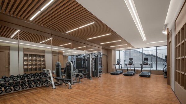 Una palestra moderna con pavimenti in legno, pareti a specchio e diverse attrezzature per l'allenamento, tra cui tapis roulant e macchinari per pesi.