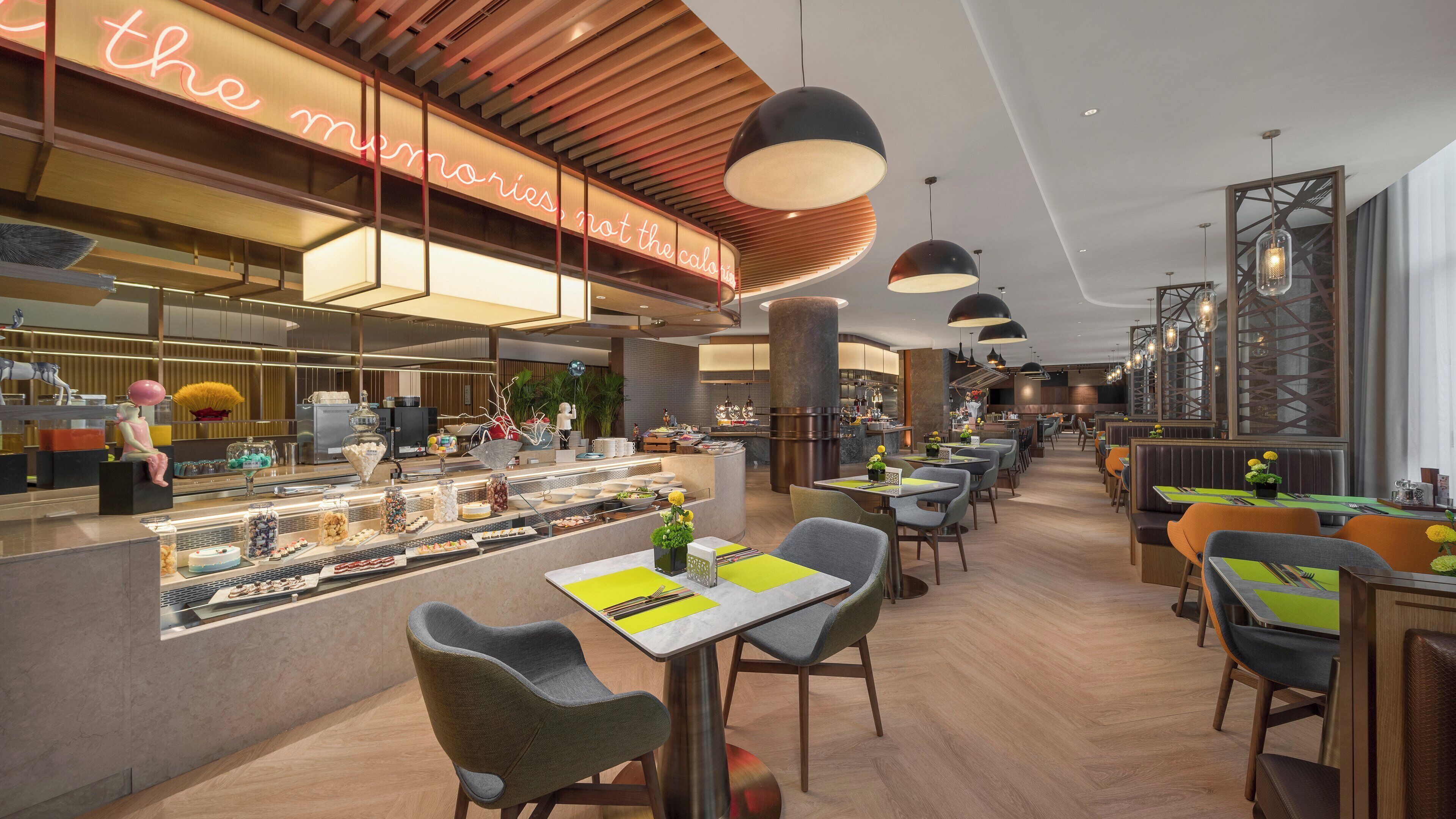 A modern restaurant with a counter displaying various food items, seating areas with tables and chairs, and a neon sign above the counter.