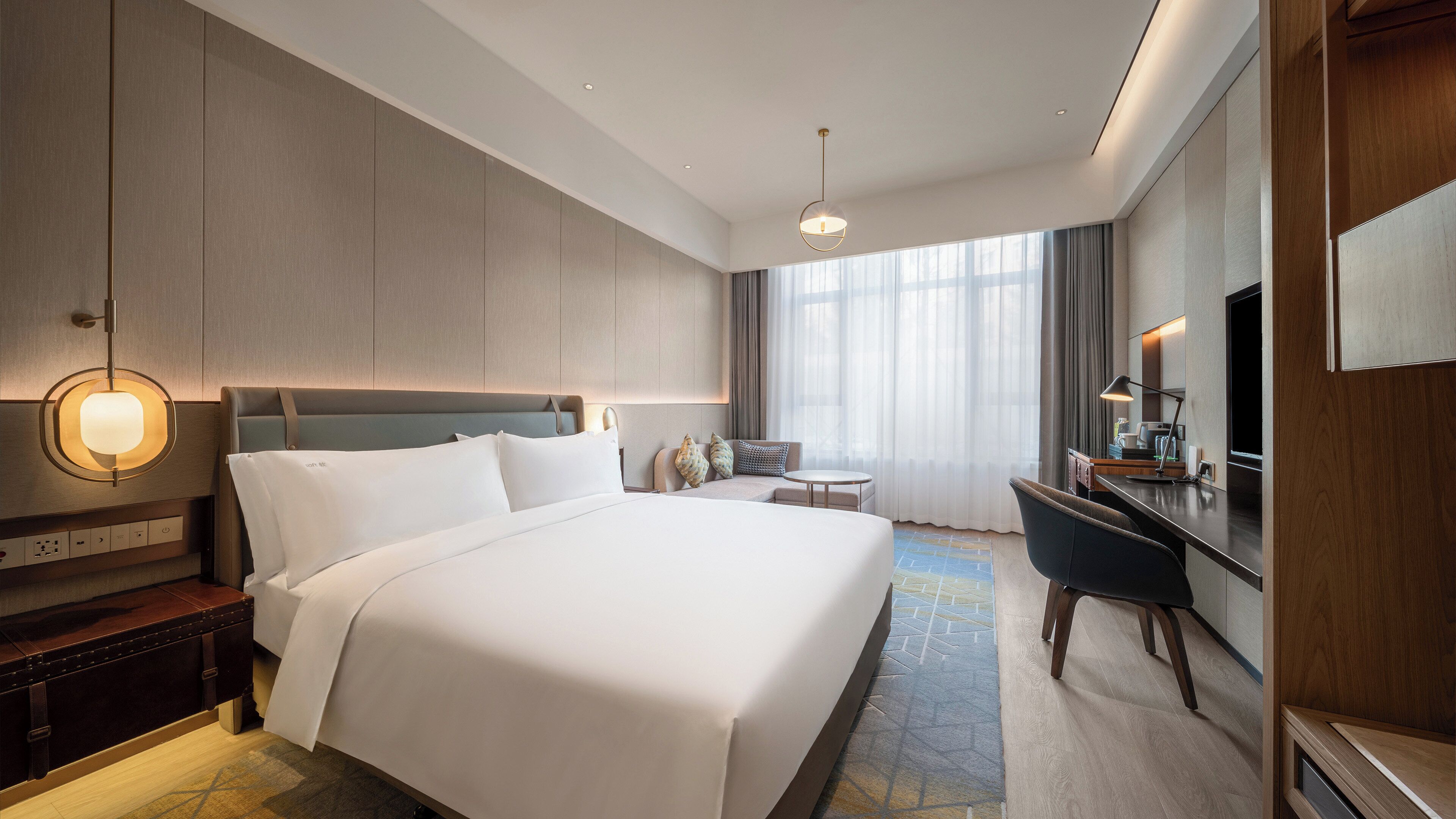 A hotel room with a large bed, a desk, a chair, a TV, and a window with curtains.