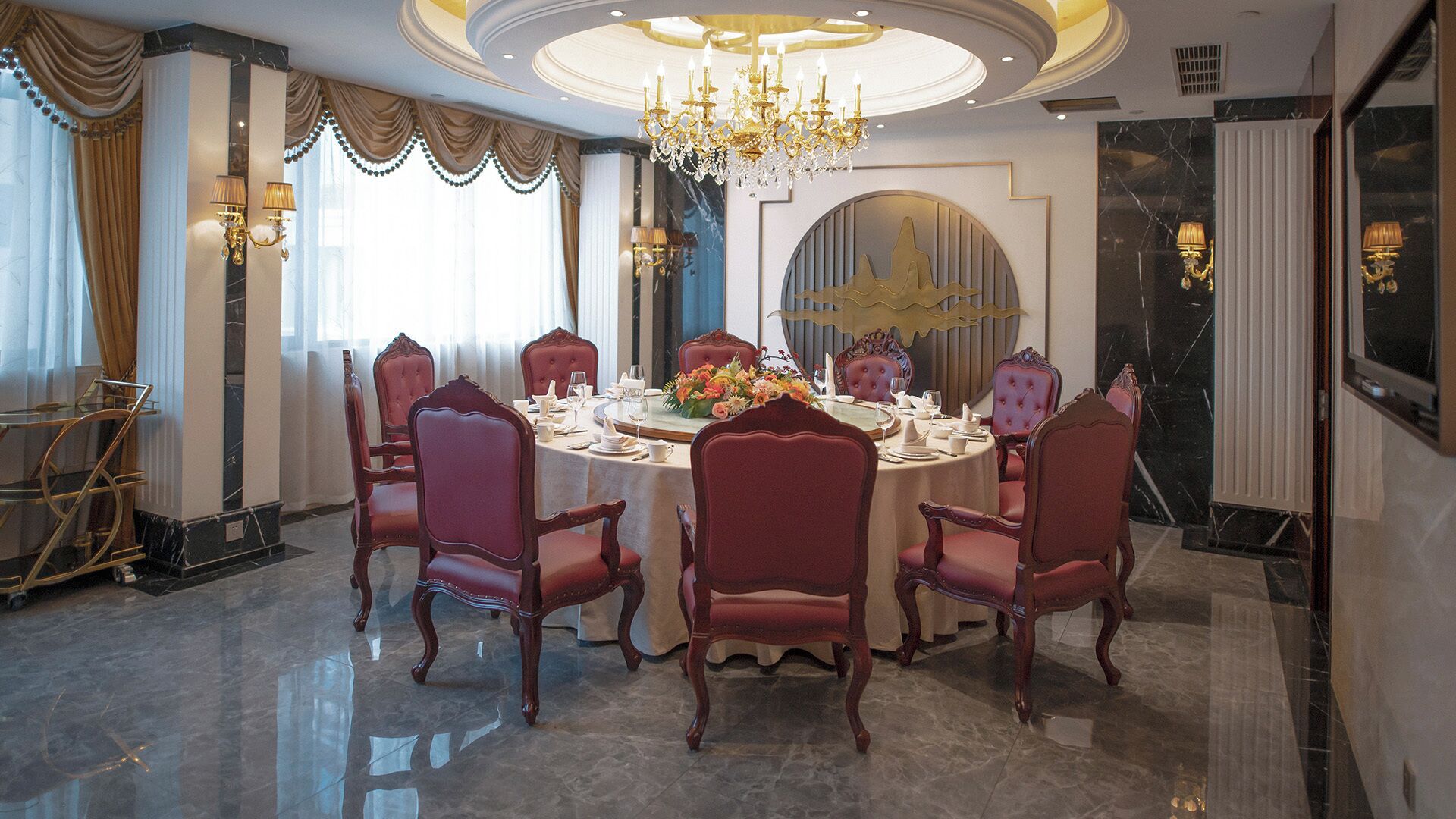 Een chique eetzaal met een ronde tafel, zes gestoffeerde stoelen, een kroonluchter en een grote spiegel aan de muur.