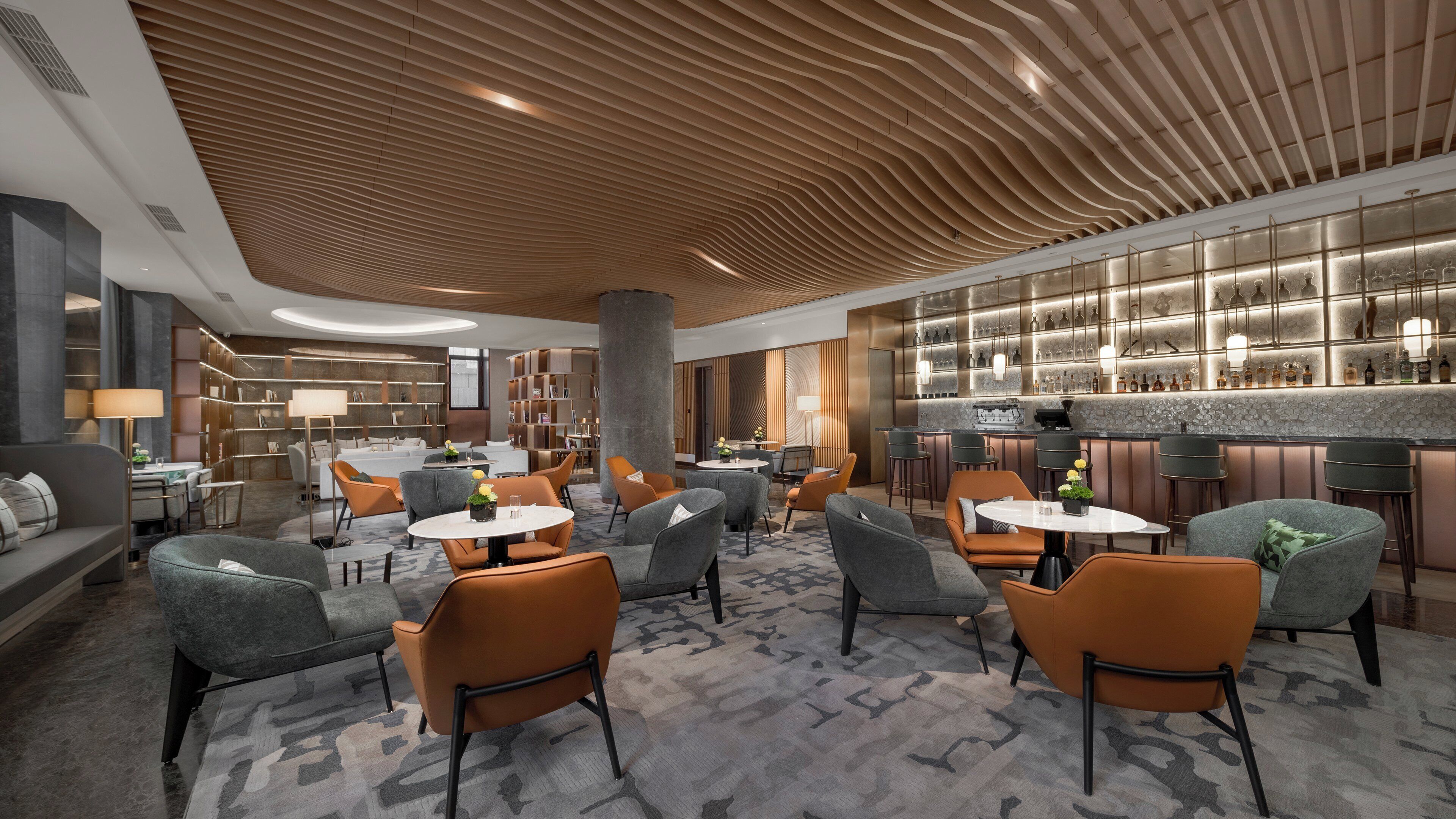 A modern hotel lobby with a bar area, seating arrangements, and a patterned carpet.