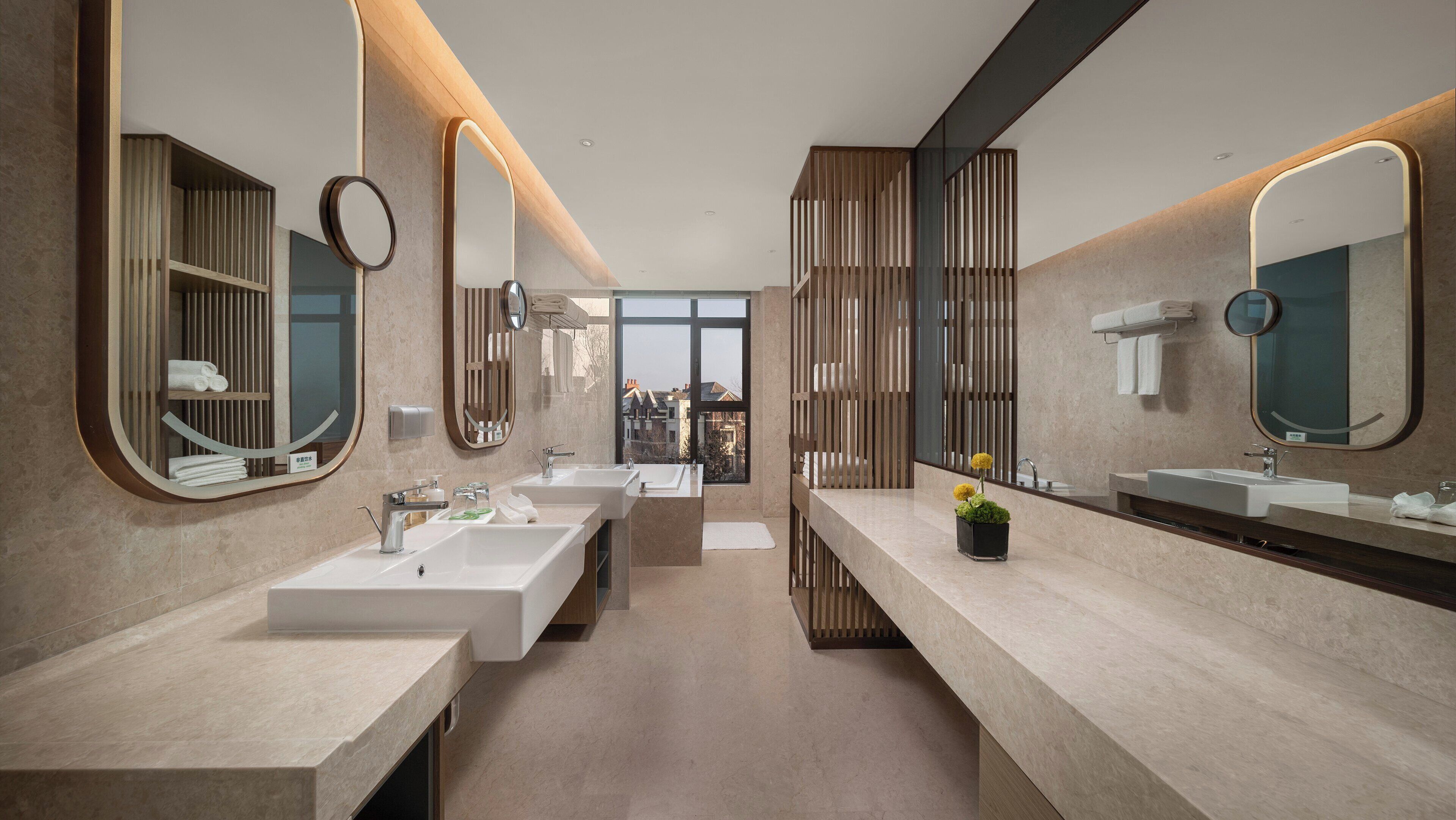 A modern bathroom with dual sinks, large mirrors, and a view of buildings through a large window.