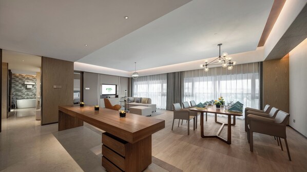 A modern hotel room with a wooden desk, a sofa, a dining table with chairs, and a TV on the wall. - Holiday Inn Changchun Jingyue by IHG (Changchun)