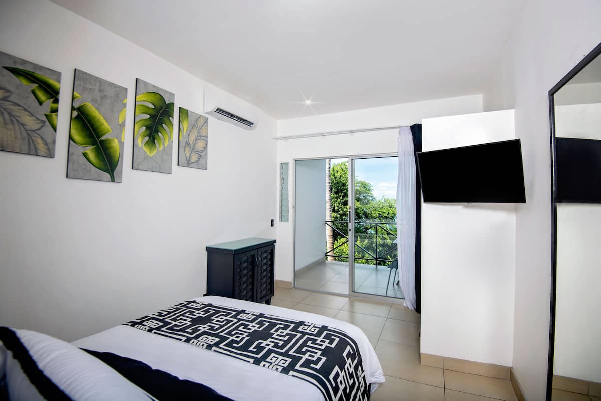 Un dormitorio con cama, televisión y balcón con vistas a zonas verdes.