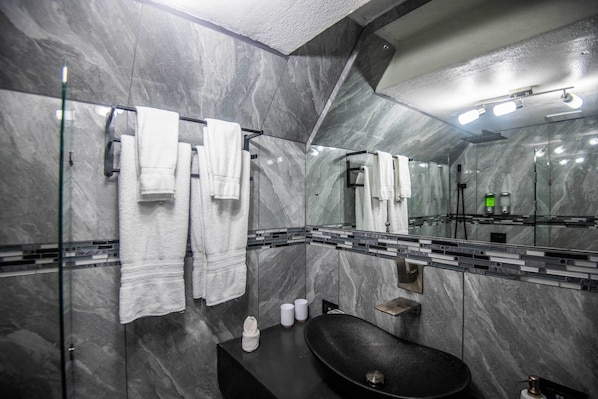 Ein modernes Badezimmer mit einem schwarzen Waschbecken, Marmorwänden und einem großen Spiegel.
