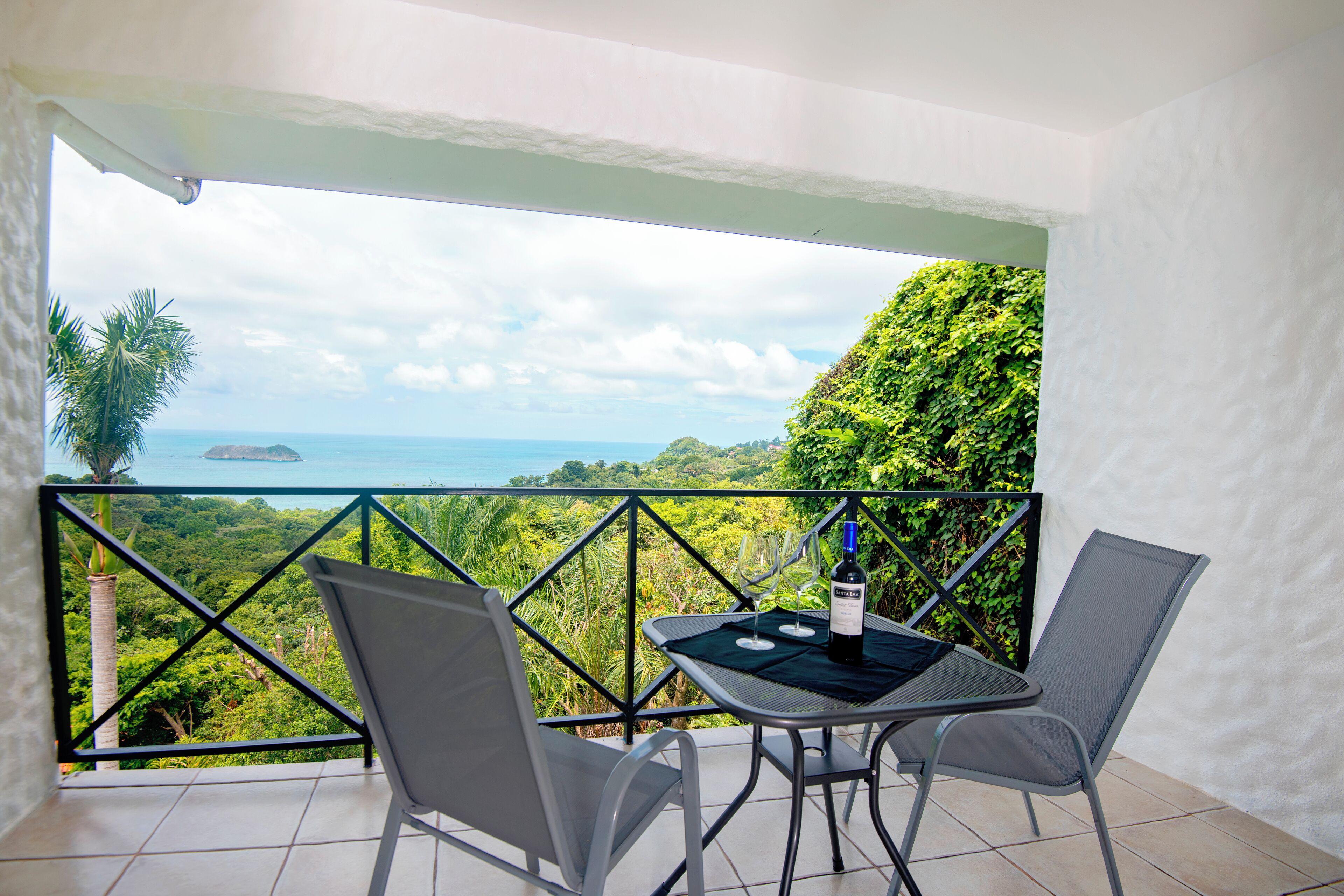 Ein Balkon mit Tisch und Stühlen, mit Blick auf eine üppige Landschaft und das Meer.