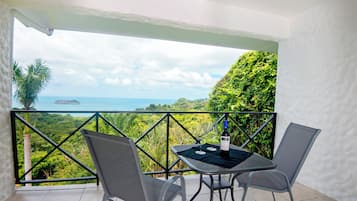 Ein Balkon mit Tisch und Stühlen, mit Blick auf eine üppige Landschaft und das Meer.