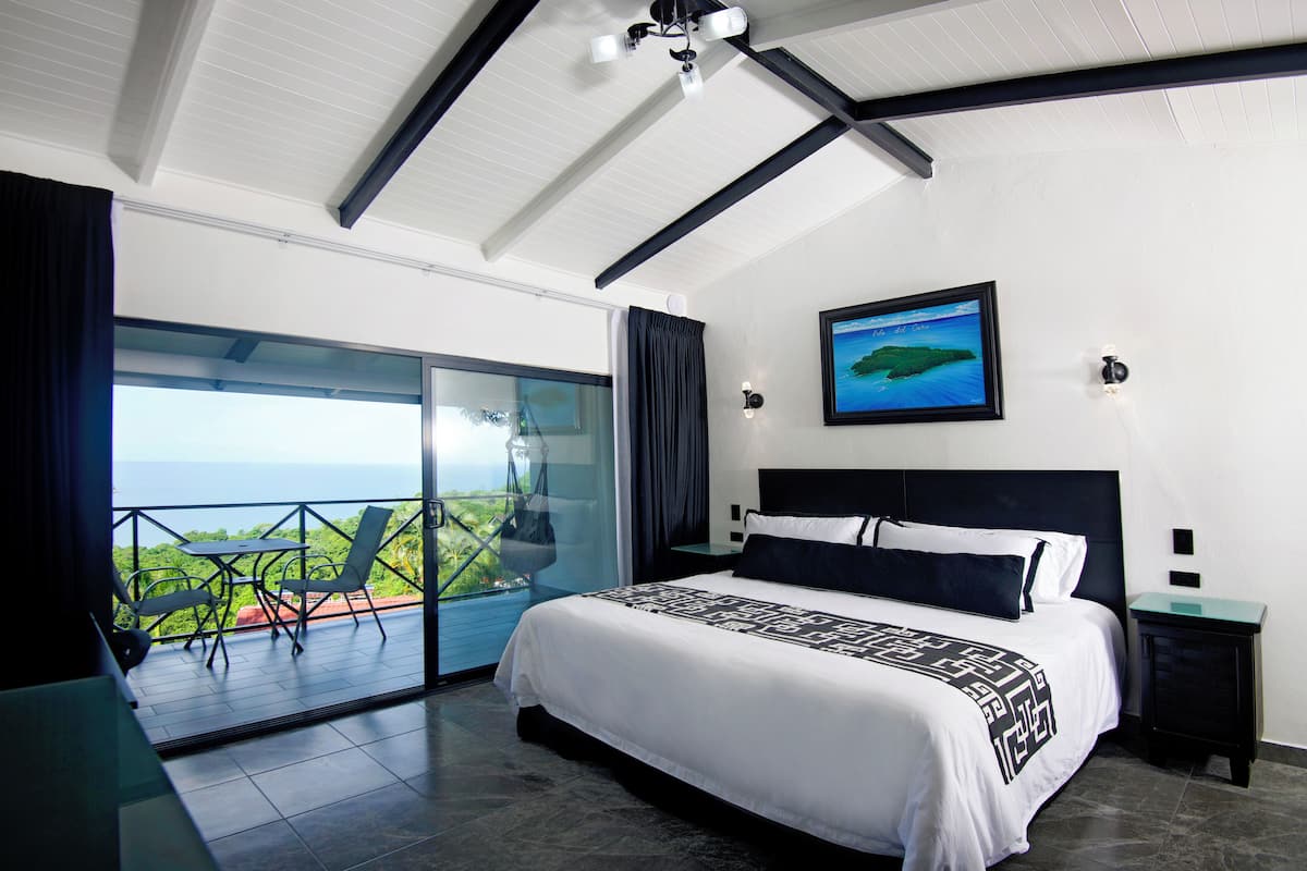 Un dormitorio moderno con una cama grande, vista al océano y balcón con mobiliario exterior.