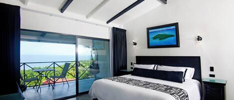 Un dormitorio moderno con una cama grande, vista al océano y balcón con mobiliario exterior.