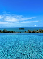 Un cielo azul despejado, una piscina con borde de azulejos y una vista distante del océano y una pequeña isla.