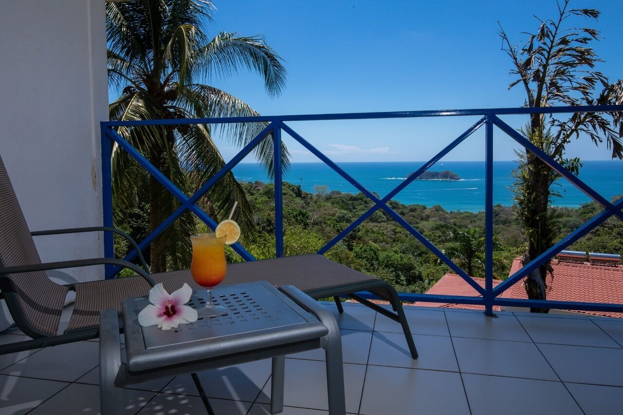 A balcony with a table, a drink, and a flower.