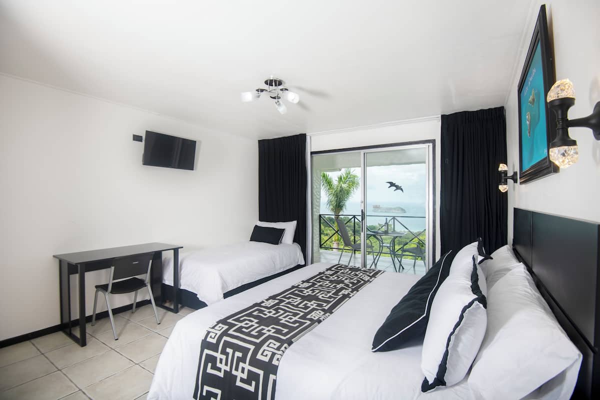 Habitación de hotel con dos camas, un escritorio, una silla, un televisor y un balcón con vistas.