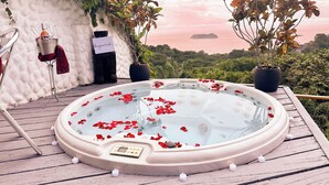 A hot tub surrounded by candles and rose petals, with a view of the ocean and greenery in the background. - Villa Roca Boutique Resort & Suites-ADULT ONLY (Quepos)