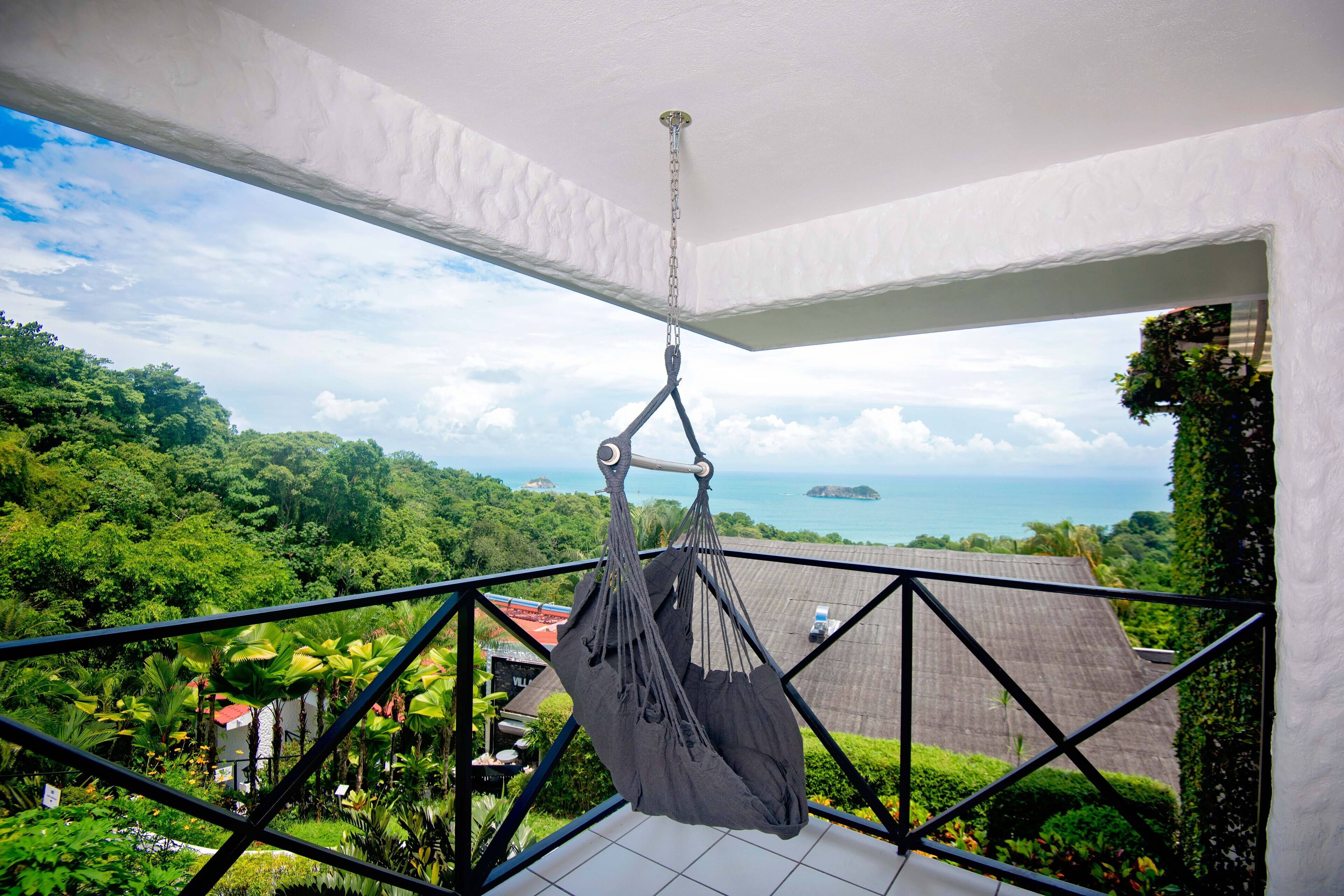 A hammock hanging from a balcony railing overlooking a lush landscape and the sea.