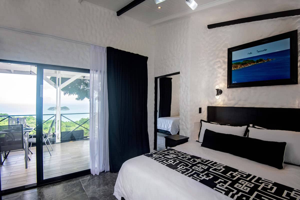 Habitación de hotel con cama, escritorio, silla y balcón con vista al mar.