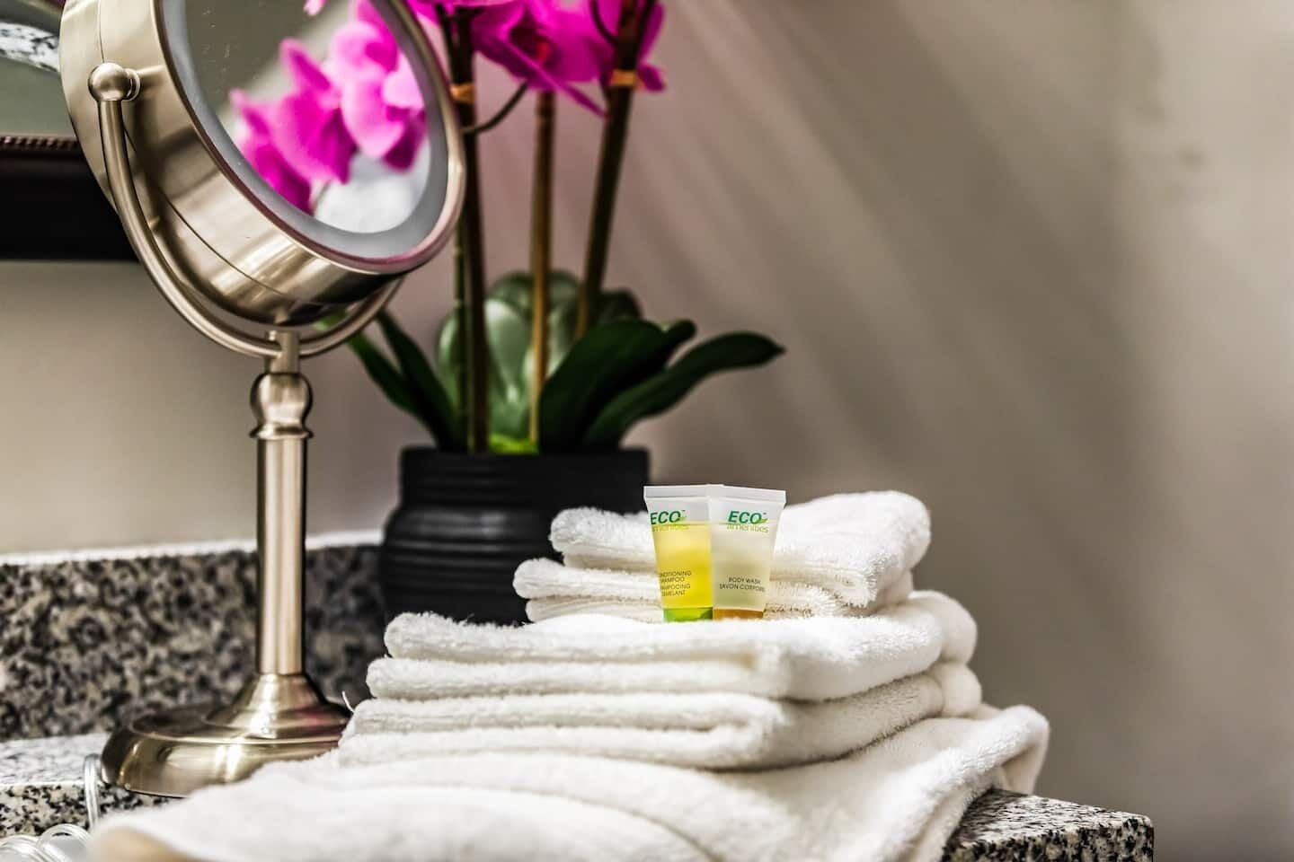 Ein Badezimmer mit Spiegel, gestapelten weißen Handtüchern und zwei Flaschen ECO Körperlotion.