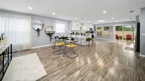 A spacious kitchen with modern appliances, a dining area with yellow chairs, and a large window with curtains.