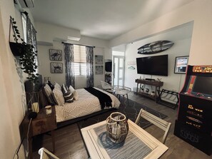 A modern living room with a sofa, a dining table with chairs, a TV, and a Pac-Man arcade machine. - Hidden gem, 4 min drive to Corcega Beach, private house (Rincon)