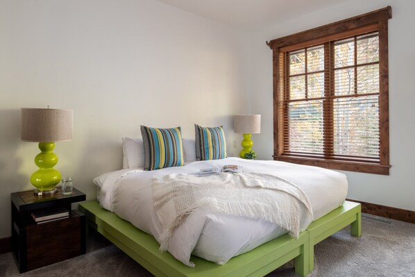A neatly arranged bedroom with a green bed, two bedside lamps, striped pillows, and a window with blinds. - Outpost: Grand View 5030 - Teton Views! (Jackson)