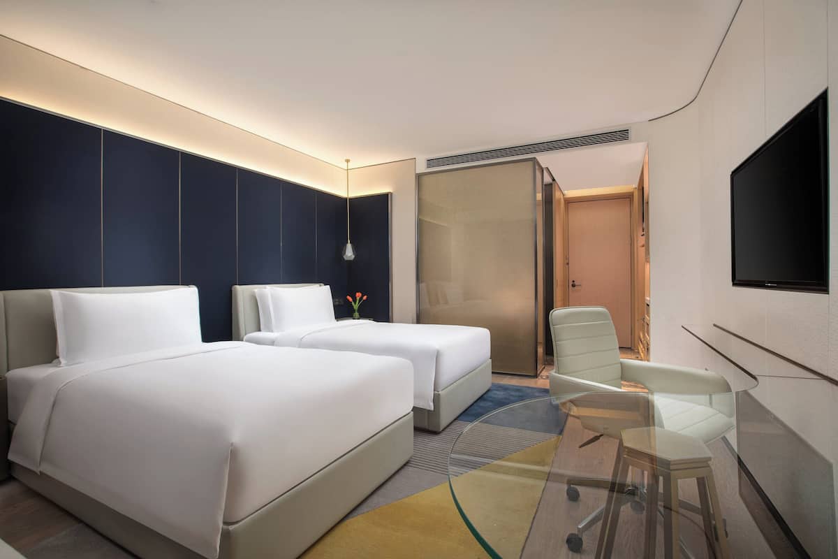 A modern hotel room with two beds, a seating area, and a TV.