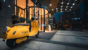 A yellow scooter parked in front of a building with a modern design and glass entrance. - voco Xi'an Etdz by IHG (Xi'an)