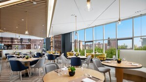 A modern restaurant with round tables, blue and gray chairs, and large windows offering city views. - voco Xi'an Etdz by IHG (Xi'an)