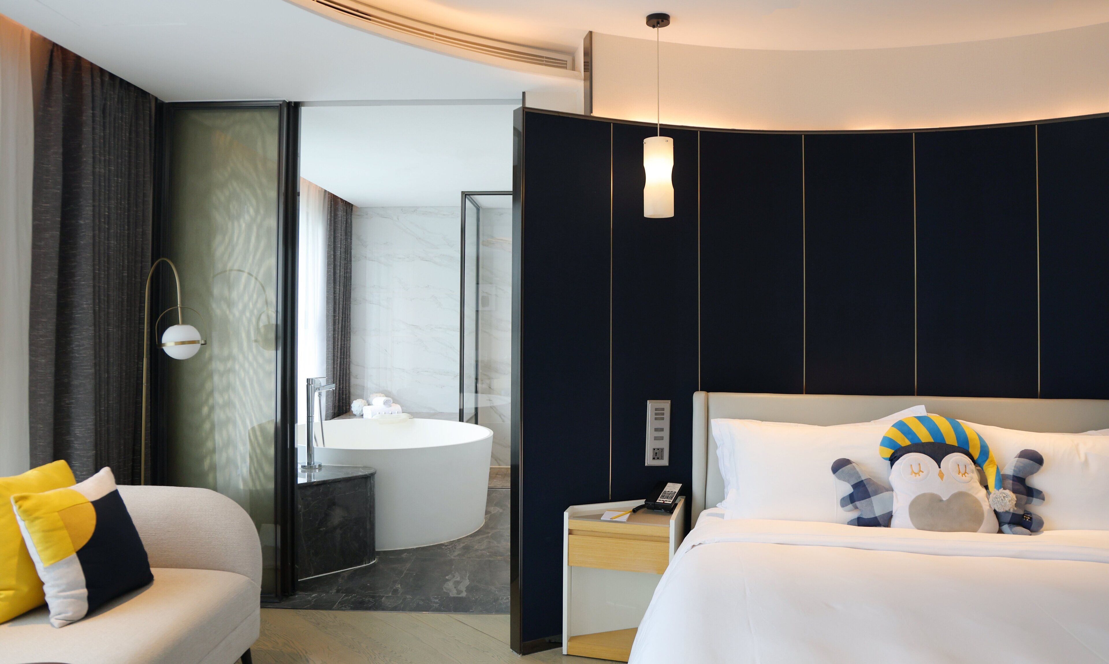 A modern hotel room with a bed, bedside table, and a bathroom with a sink and mirror.