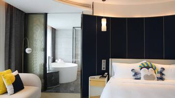 A modern hotel room with a bed, bedside table, and a bathroom with a sink and mirror.