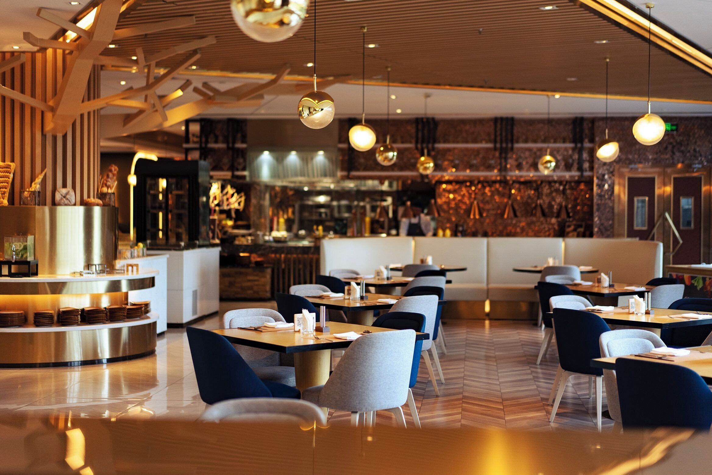 Ein modernes Restaurant mit runden Tischen, blau-grauen Stühlen und schwebenden, kugelförmigen Lampen.