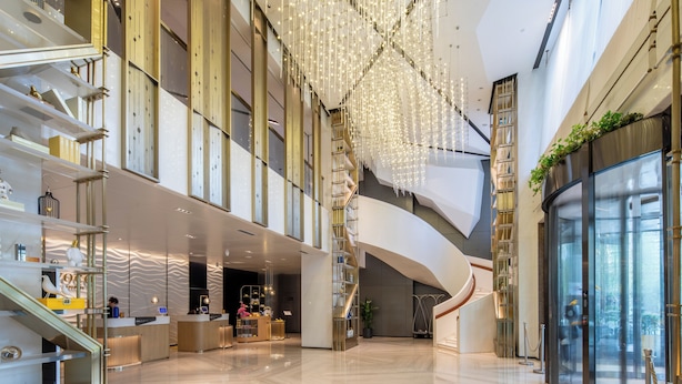 A spacious lobby with a modern design, featuring a central staircase, a reception desk, and a glass elevator. - voco Xi'an Etdz by IHG (Xi'an)