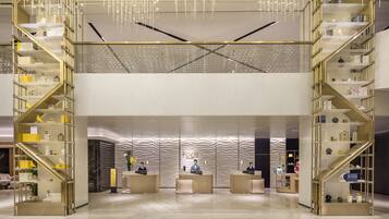 A modern hotel lobby with a central reception desk, two symmetrical staircases, and a decorative ceiling.