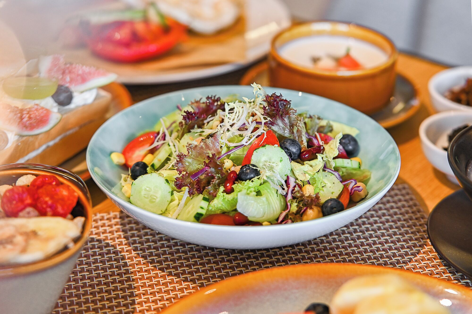 A table with a bowl of salad, a bowl of soup, and a plate with sliced tomatoes.