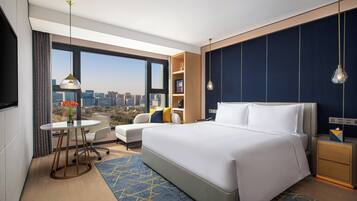 A modern hotel room with a large bed, a desk, and a view of the city.