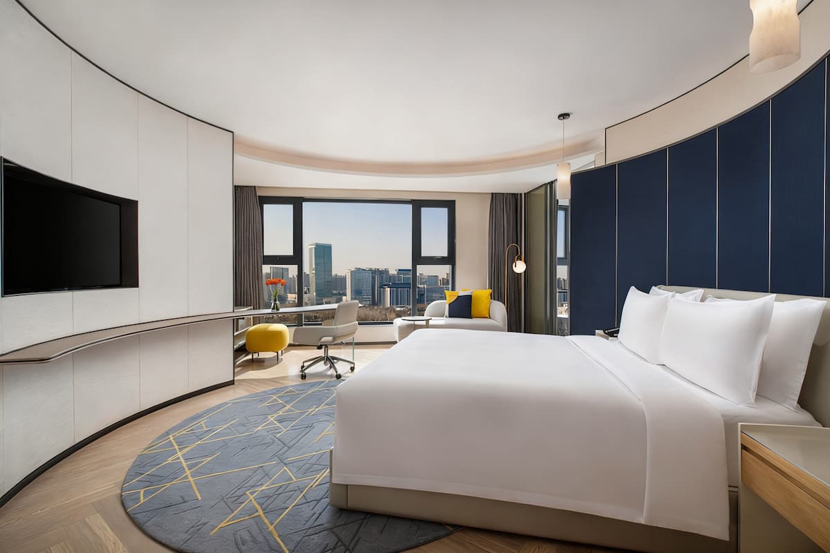 A modern hotel room with a large bed, a desk, a chair, and a TV.