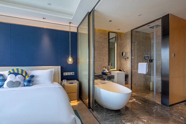 A modern hotel room with a large bed, a bathtub, a walk-in shower, and a bathroom with a mirror and sink.