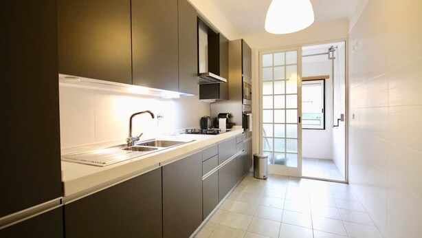 A modern kitchen with a long countertop, stainless steel sink, and a hanging light fixture.