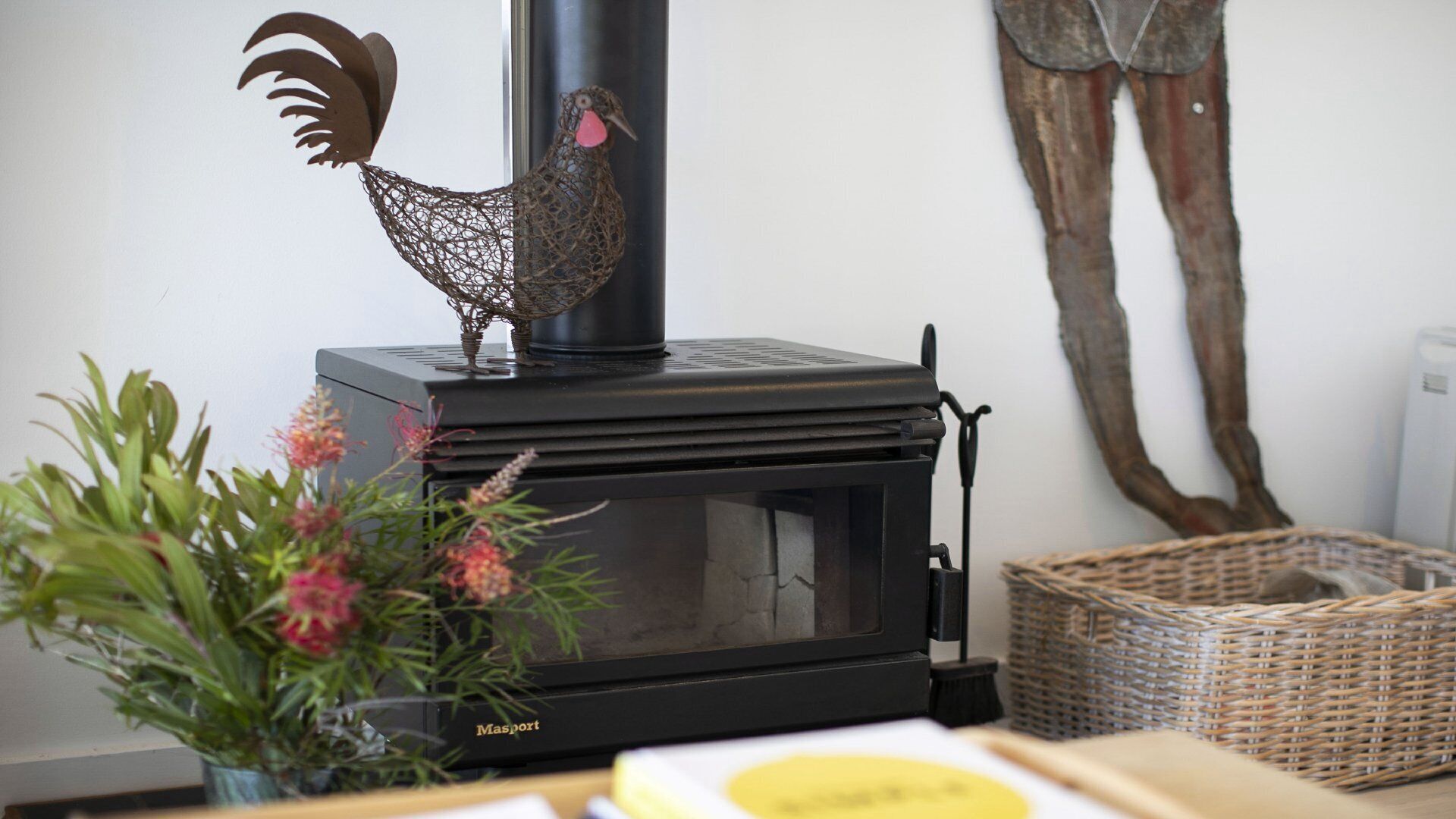 A wood-burning stove with a rooster decoration, a potted plant, and a woven basket.