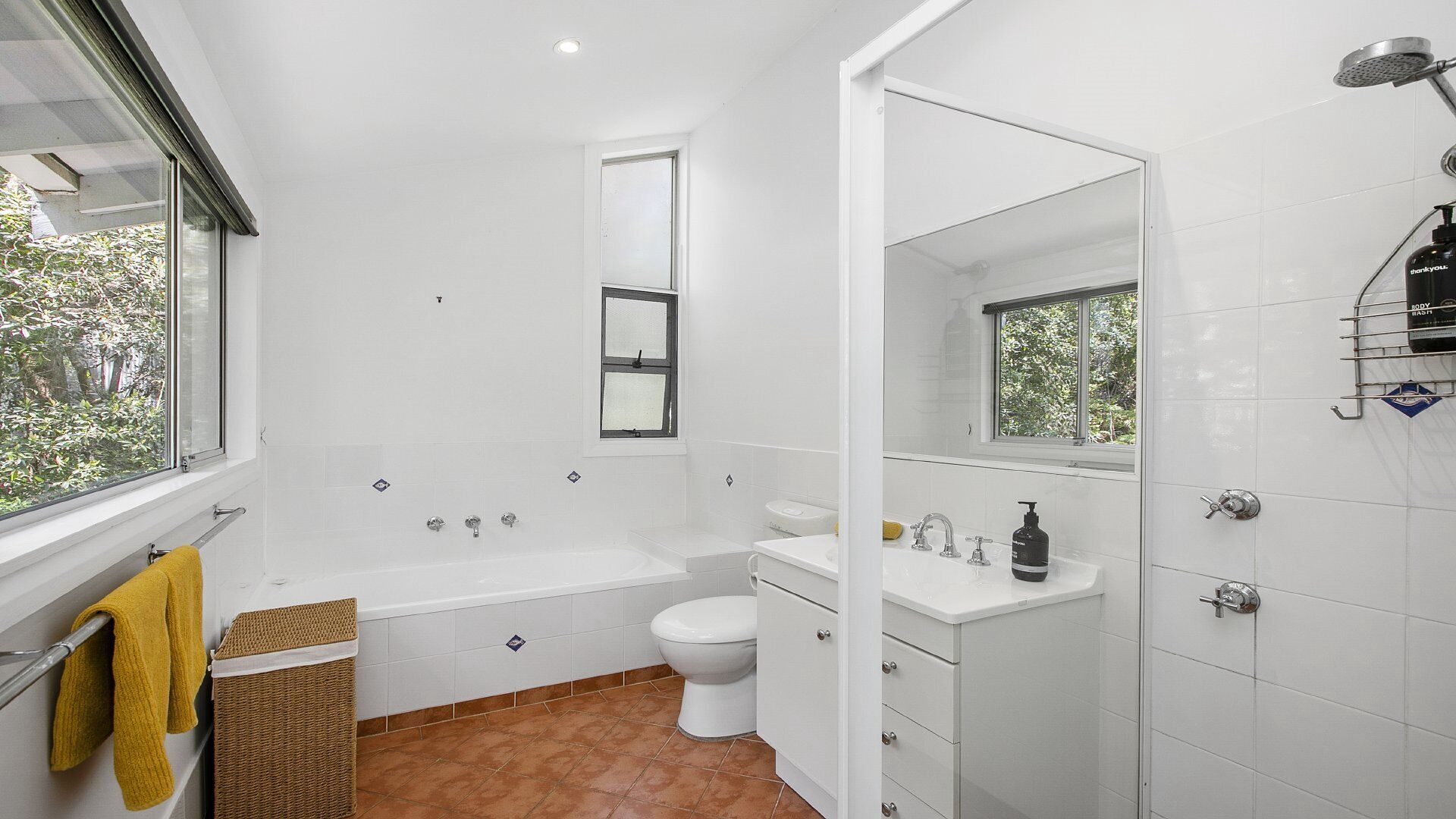A modern bathroom with a bathtub, toilet, and sink, featuring a large window and a shower area.