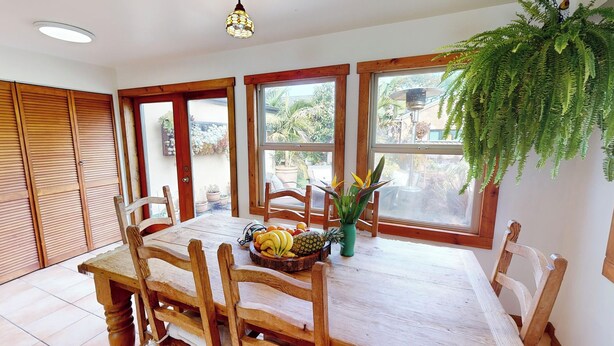 A dining area with a wooden table and chairs, a fruit basket, and a hanging plant.