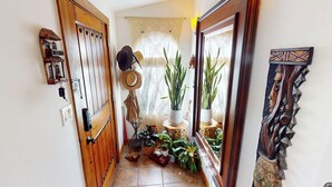 A narrow hallway with a wooden door, a wall-mounted hat rack, and a window with lace curtains.