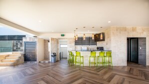 A spacious kitchen with a herringbone wood floor, a bar area with green chairs, and a modern design with stone walls and recessed lighting.