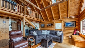 Interior de cabana de tronco com escada de madeira, poltrona de couro, sofá seccional e escrivaninha de madeira.