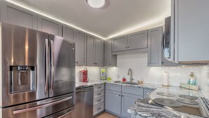 A modern kitchen with stainless steel appliances, grey cabinets, and a granite countertop. - DIRECT OCEANFRONT BEACH HOME! PRIVATE BEACH ACCESS! (New Smyrna Beach)
